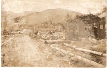 Lesno skladišče ob parni žagi GAJ in verjetno spodnja postaja tovorne žičnice na razglednici iz časa okoli 1915, ki jo je prizadel zob časa (hrani avtor) title=